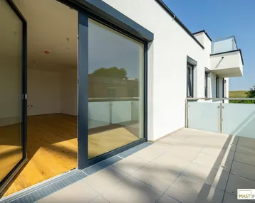 Heller Balkon mit Fliesenboden und Glasgeländer, bietet Zugang zu einem lichtdurchfluteten Innenraum.
