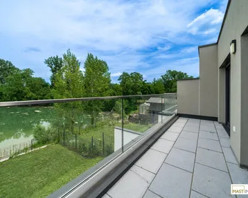 Großer Balkon mit Glasgeländer, Fliesenboden und malerischem Blick auf den See.