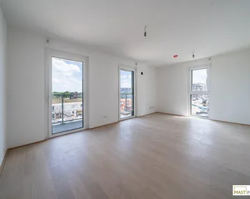 Helles Zimmer mit Holzboden und Zugang zu mehreren Fenstern, Blick auf eine Baustelle.