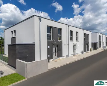 Moderne Reihenhäuser mit weißer Fassade und dunklen Akzenten unter blauem Himmel.
