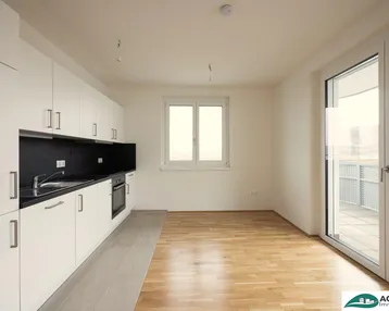 Moderne Küche mit weißen Schränken, schwarzer Arbeitsplatte und Zugang zu einem Balkon.
