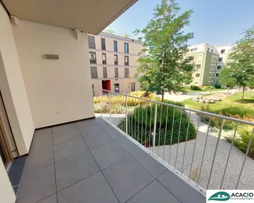 Heller Balkon mit modernen Fliesen und Blick auf die gepflegte Grünanlage und umliegende Gebäude.