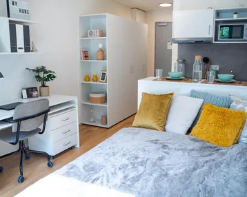 Helles Studio-Apartment mit Bett, Schreibtisch und integrierter Küchenzeile, ideal für Studenten.