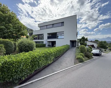 Modernes Mehrfamilienhaus mit gepflegter Grünanlage und Zufahrt von der Straße.
