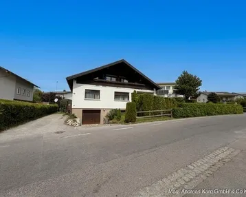 Einfamilienhaus mit Satteldach, Garage im Untergeschoss und gepflegter Hecke an der Straße.