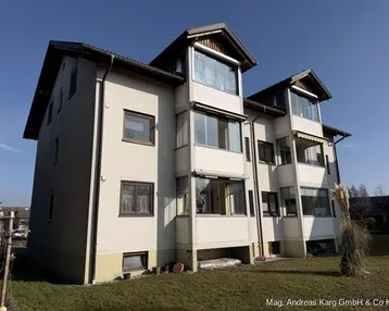 Mehrfamilienhaus mit mehreren Etagen, Balkonen und großen Fenstern unter blauem Himmel.