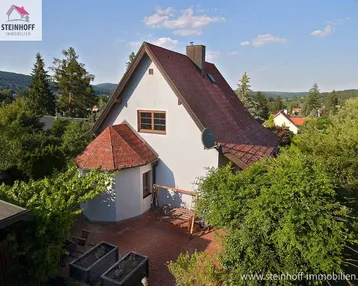 Freistehendes Einfamilienhaus mit rotem Ziegeldach und umgebender grüner Landschaft unter blauem Himmel.