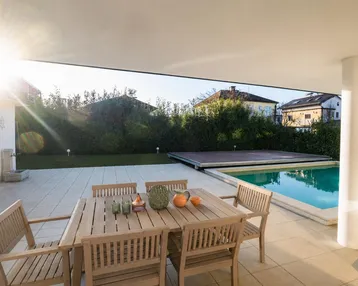 Sonnige Terrasse mit Esstisch, Stühlen und einem erfrischenden Pool, umgeben von Grün.