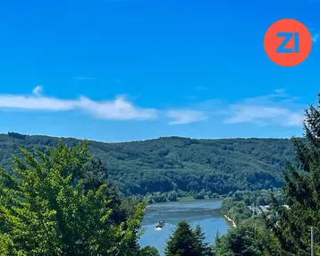 Malerischer Ausblick auf den Fluss, der sich durch bewaldete Hügel schlängelt, unter strahlend blauem Himmel.