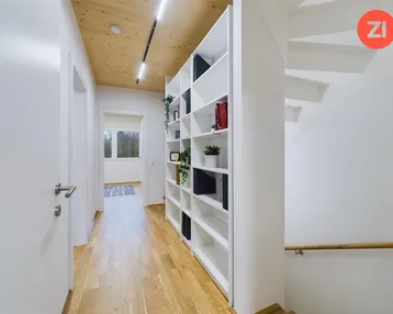 Heller Flur mit Holzdecke, Einbauregal und Zugang zu einer Treppe.