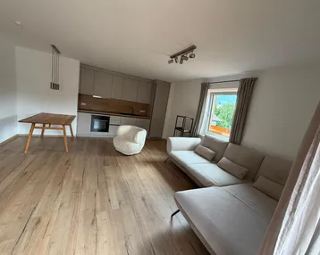 Heller offener Wohn- und Essbereich mit moderner Küche und Holzboden, bietet einen grünen Ausblick.