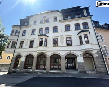 Historisches Gebäude mit heller Fassade, vielen Bogenfenstern und Arkaden im Erdgeschoss.