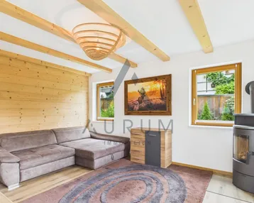 Helles Wohnzimmer im alpinen Stil mit Holzbalken, Kaminofen und gemütlichem Sofa.