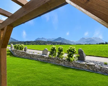Blick auf die Berge über eine grüne Wiese mit einer Holzpergola im Vordergrund.