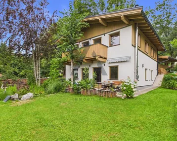 Hausfassade mit gepflegtem Garten, Rasenfläche und kleinen Blumenbeeten.