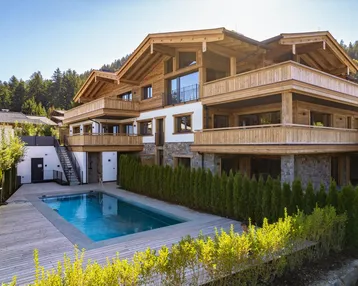 Luxuriöses Chalet mit Außenpool und Holzfassade, umgeben von grüner Natur und Bergen.