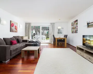 Heller Wohn- und Essbereich mit bequemer Couch, Fernseher und Zugang zur Terrasse mit Gartenblick.