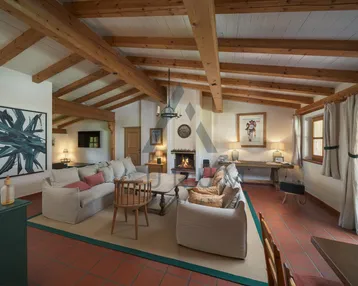 Gemütliches Wohnzimmer mit Kamin, sichtbaren Holzbalken und Terrakottaboden, ideal für entspannte Abende.