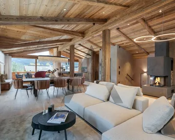 Geräumiger Wohn-Essbereich im Chalet-Stil mit Holzbalkendecke, Kamin und Zugang zum Balkon mit Bergblick.