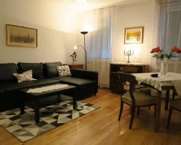 Gemütlicher Wohn- und Essbereich mit dunklem Sofa, Esstisch und hellem Parkettboden.