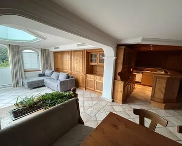 Geräumiger Wohn- und Essbereich mit traditionellen Holzmöbeln, Fliesenboden und viel Tageslicht durch große Fenster.