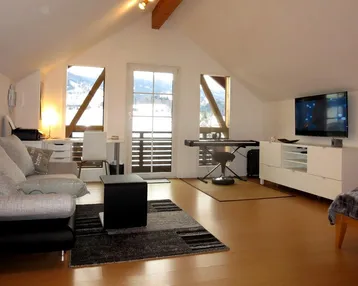 Geräumiger Wohnbereich im Dachgeschoss mit Holzboden, Sofa und Zugang zum Balkon.