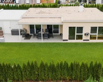 Luftaufnahme eines modernen Einfamilienhauses mit großem Garten und überdachter Terrasse.