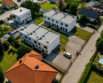 Luftaufnahme von modernen Reihenhäusern mit Flachdächern und umliegenden Grünflächen in einer Wohnsiedlung.