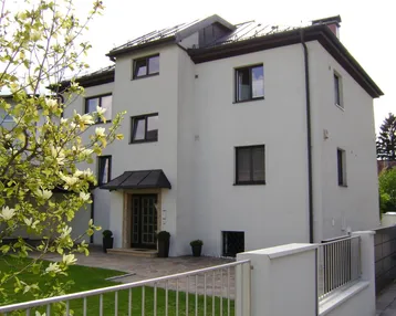 Modernes Wohnhaus mit weißer Fassade, dunklen Fenstern und gepflegtem Vorgarten.