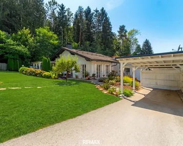 Haus mit großem Garten, gepflegtem Rasen und einem Carport unter blauem Himmel.