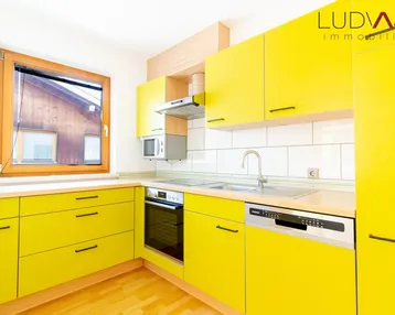 Moderne Küche mit leuchtend gelben Schränken, integrierten Geräten und Fenster.