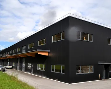 Modernes Geschäftsgebäude mit schwarzer Fassade, großen Fenstern und Holzelementen unter einem Vordach.