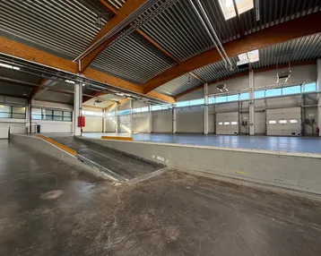 Geräumige Lagerhalle mit Laderampe, hohen Decken, Holzträgern und Rolltoren für einfachen Zugang.