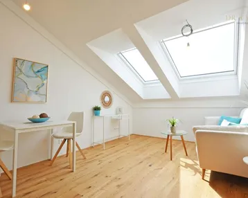 Helles Dachgeschoss-Wohnzimmer mit großen Dachfenstern, Holzboden und moderner Einrichtung.