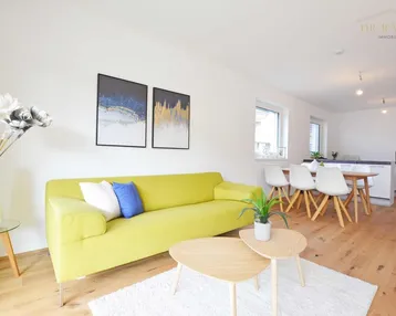 Helles, offenes Wohn- und Esszimmer mit moderner Einrichtung, Holzboden und integrierter Küchenzeile.