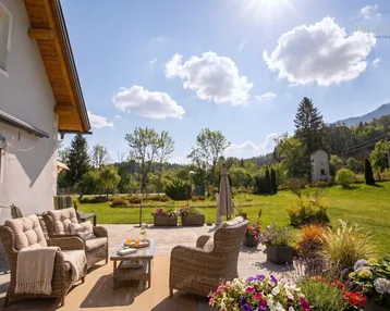 Sonnige Terrasse mit bequemen Korbmöbeln, Blumen und weitem Blick ins Grüne und auf die Berge.