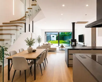 Moderner offener Wohn-Essbereich mit Holzboden, eleganter Treppe und Blick in den Garten.