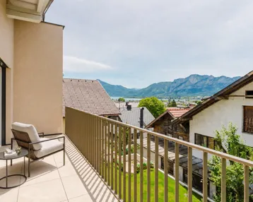 Großer Balkon mit Sitzgelegenheiten und atemberaubendem Blick auf See und Berge.