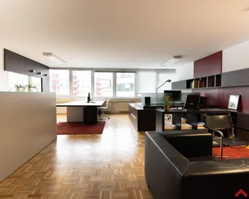 Geräumiges und helles Büro mit mehreren Arbeitsplätzen, Holzparkettboden und großen Fenstern.