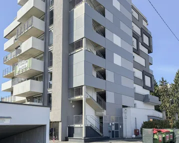 Modernes Mehrfamilienhaus mit mehreren Balkonen und einer Tiefgaragenzufahrt.