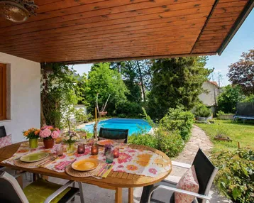 Überdachte Terrasse mit Esstisch und Blick auf den Garten mit privatem Pool und Trampolin.