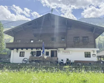 Traditionelles Holzhaus in den Bergen mit Balkonen und weiß getünchter Fassade, umgeben von grüner Natur.