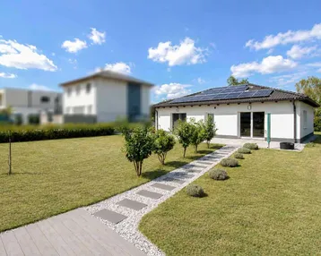 Modernes Einfamilienhaus mit gepflegtem Garten und Solaranlage auf dem Dach unter blauem Himmel.