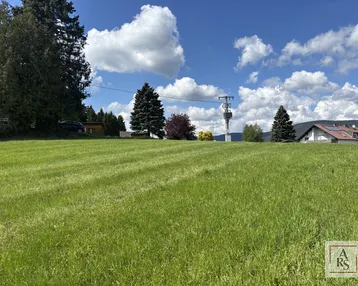 Weitläufige grüne Wiese mit Blick auf die umliegende Landschaft, Berge und ein Haus mit Solaranlage.