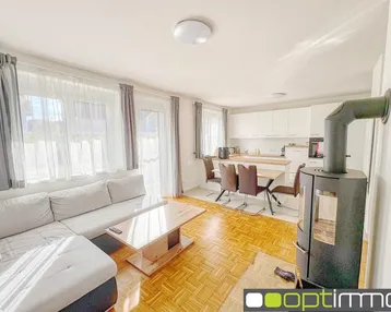 Heller offener Wohn-Essbereich mit Holzboden, Kaminofen und Zugang zum Balkon.