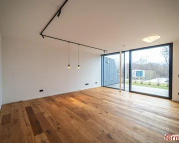 Heller, leerer Raum mit Holzboden und großen Fenstern, die viel Tageslicht hereinlassen.