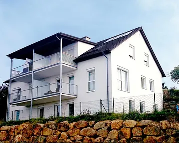 Modernes Mehrfamilienhaus mit weißer Fassade, Satteldach und mehreren Balkonen mit Metallgeländer.