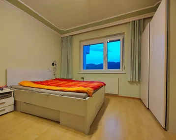 Helles Schlafzimmer mit Doppelbett, Kleiderschrank und Blick auf die Landschaft.