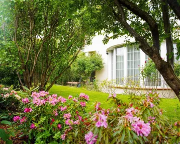 Gepflegter Garten mit blühenden Rhododendren und Blick auf die Hausfassade mit großen Fenstern.