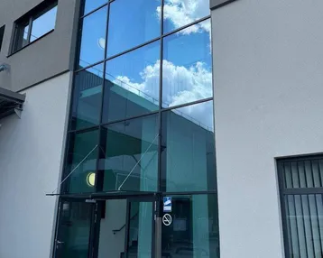 Moderne Gebäudefassade mit großer Glasfront und Eingangsbereich unter blauem Himmel.